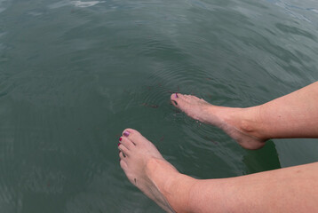 Close up to a woman feet inside a green blue lake with small fishes swiming around feet 