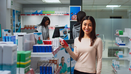 Asian client checking medicine boxes on drugstore shelves, looking at packages to find treatment and pills. Reading leaflets to buy supplements and pharmaceutical products at medical store.