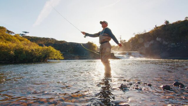 Fisherman casts the line on a river at sunrise. Angler stands in waders in the river and fishing on fly