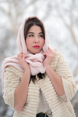 Charming brunette woman with red plump lips dressed in three-quarter sleeve fur coat and pink scarf on head looking away on winter day outdoors. Shallow depth of field, selective focus on foreground