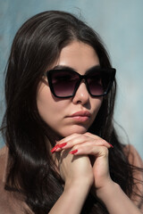 Face of fashionable young hipster with plump lips and black long hair looking thoughtfully at camera through dark sunglasses. Sulking young adult female model