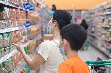 Asian mother and son shopping in a department store during a pandemic, wearing a surgical face mask to prevent coronavirus or covid-19, shopping concept.