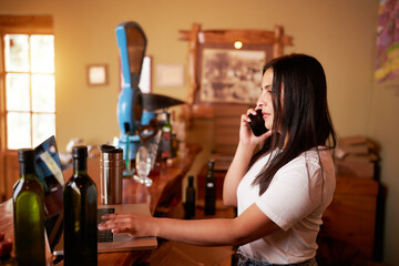 Latin woman talking on the cell phone in front of her laptop and selling online merchandise in her small olive oil business 