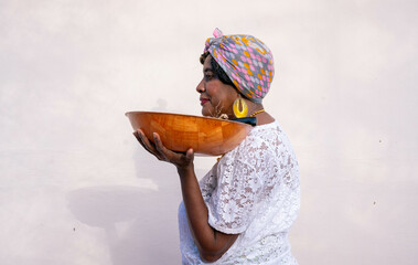 Caribbean woman wearing headwrap holding a bowl of sugar cane