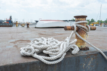 heavy cotton nautical rope, still wet and salty from recent use, tying large commercial fishing trawler boat vessels to the iron pilons of downtown seaport dock while moored at port