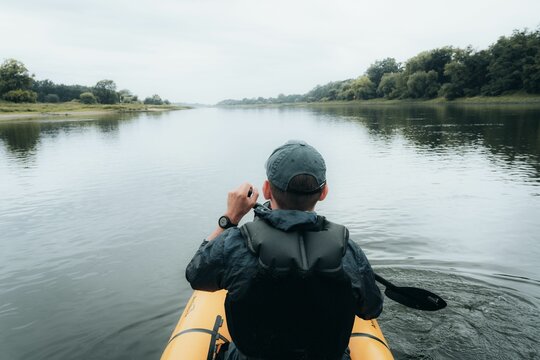 Back view of a young man paddling with packraft on a river