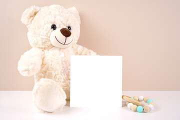 Square vertical greeting card party invitation product mockup. Baby shower birthday christening gender neutral. Styled with white teddy bear against a beige and white background. Negative copy space.