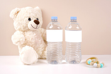 Water bottle labels product mockup. Baby shower 1st birthday christening gender neutral party theme. Styled setting with white teddy bear against a beige and white background. Negative copy space.
