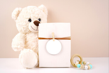 Gift with round thank you favor card tag product mockup. Baby shower 1st birthday christening gender neutral. Styled with white teddy bear against a beige and white background. Negative copy space.