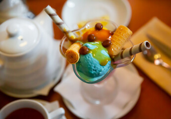 Balls of yellow and blue ice cream with waffle tube in glass ramekin on table. Top view