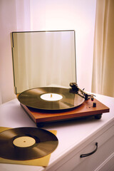 Stylish turntable and vinyl records on white chest of drawers indoors