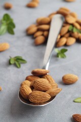 Spoon with tasty almonds and fresh green leaves on light grey table, closeup