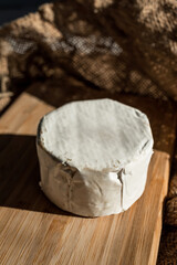 A composition of a round cheese head with white mold on a bamboo board on a background of burlap. Aesthetic serving of food