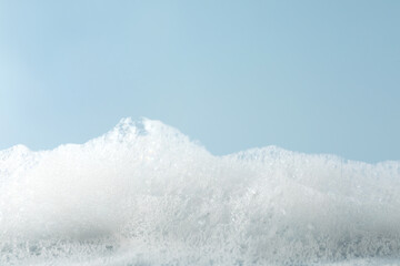 Fluffy bath foam on light blue background, closeup. Space for text