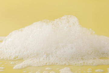 Fluffy bath foam on pale orange background, closeup