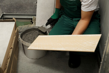 Worker applying adhesive mix on ceramic tile with spatula, closeup