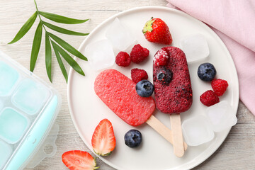 Plate of tasty berry ice pops on light wooden table, flat lay. Fruit popsicle