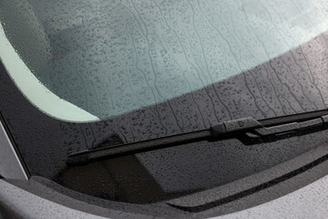 Car wiper cleaning water drops from windshield glass, closeup