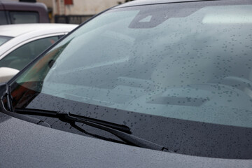 Car wiper cleaning water drops from windshield glass, closeup