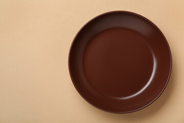 Empty brown ceramic plate on pale orange background, top view. Space for text