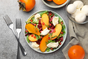 Delicious persimmon salad with cheese and pomegranate served on grey table, flat lay