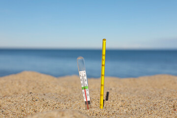 Different weather thermometers in sand near sea