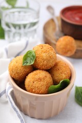 Bowl of delicious fried tofu balls with basil on white table, closeup