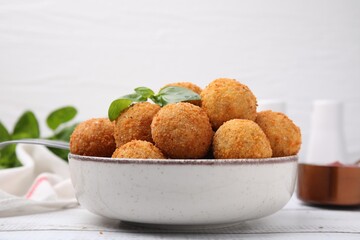 Bowl of delicious fried tofu balls with basil on white wooden table