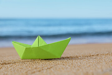 Fototapeta na wymiar Light green paper boat near sea on sandy beach, space for text