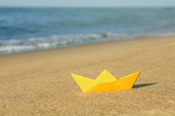 Fototapeta na wymiar Yellow paper boat near sea on sandy beach, space for text