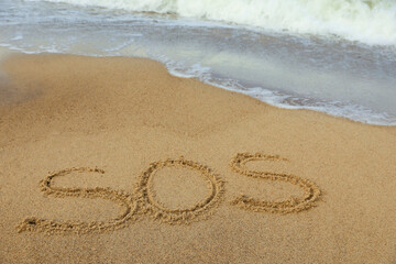 Message SOS drawn on sand near sea