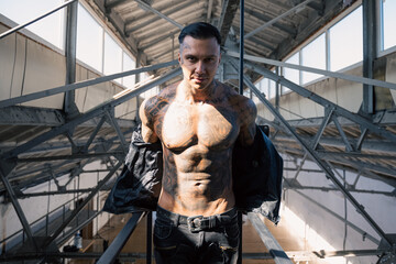 hot tattooed man in leather against the big window.Handsome Young Athletic Male Fashion Model.Muscular athletic sexy male with naked torso. Brutal handsome man with tattooed body.