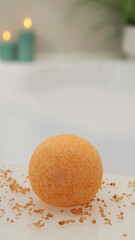 Orange bath bomb with salt on countertop near tub indoors. Bokeh effect