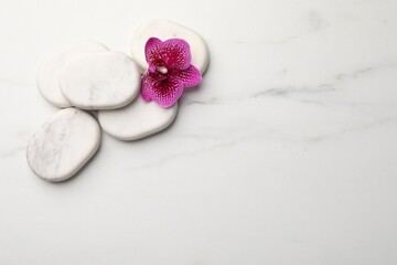 Flat lay composition with spa stones and orchid on white marble table. Space for text