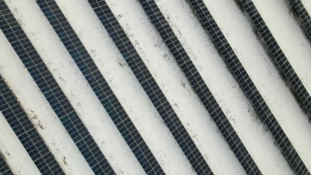 Aerial view of electrical power plant with solar panels covered with snow melting down in winter end for producing clean energy. Concept of low effectivity of renewable electricity in northern region