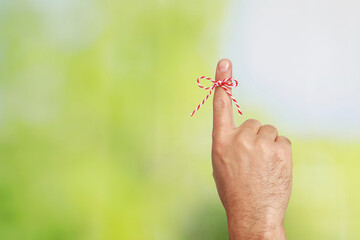 Man showing index finger with tied bow as reminder on green blurred background, closeup. Space for text