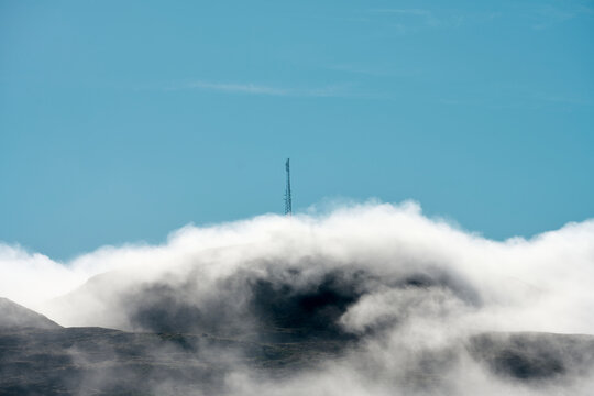 Blue sky over mountain with high tower covered with mist