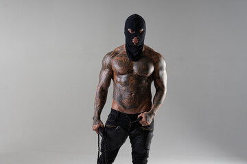 Obraz premium Muscular shirtless young man with whip in a mask.Brutal handsome man with tattooed body. Men tattoo casual fashion. Portrait of handsome male model. Muscular athletic sexy male with naked torso.