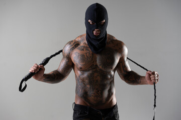 Muscular shirtless young man with whip in a mask.Brutal handsome man with tattooed body. Men tattoo...