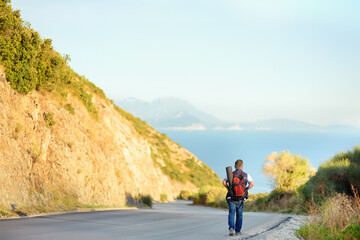 Mature man hiking on mountains nearby sea. Person walking along road. Concepts of adventure, extreme survival, orienteering. Hitch-hiking. Solo travel. Backpacking trip.