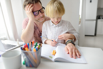 Tired father helping school boy with ADHD do his homework at home. Homeschooling, distance learning, online studying, remote education for kids.