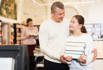 Positive little girl with her loving father holding pile of books bought in bookshop. Focus on man