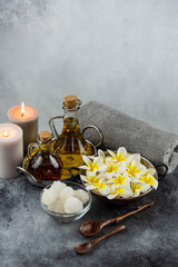 Fototapeta na wymiar Spa massage relax composition setting. Natural essence oils, sea salt, towel, candles and plumeria frangipani exotic flowers. Gray colors.