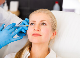 Fototapeta premium Cosmetologist making injections of botulotoxin in face of young woman.