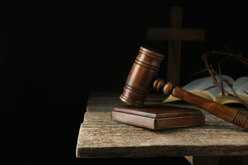 Judge gavel, bible, cross and crown of thorns on wooden table against black background. Space for...