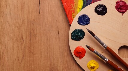 Artist's palette with samples of colorful paints and brushes on wooden table, flat lay. Space for text