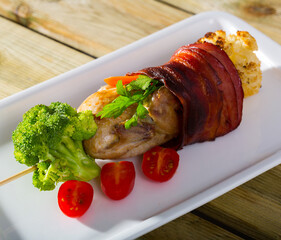 Grilled quail with jamon, fried on skewers with brocolli and tomatoes at plate