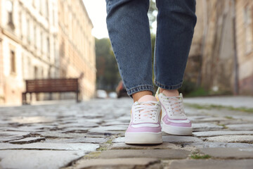 Woman in stylish sneakers walking on city street, closeup