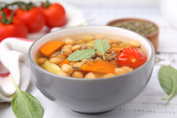 Tasty chickpea soup in bowl and spices on white wooden table, closeup