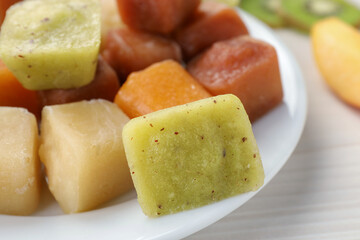 Different frozen fruit puree cubes on white wooden table, closeup